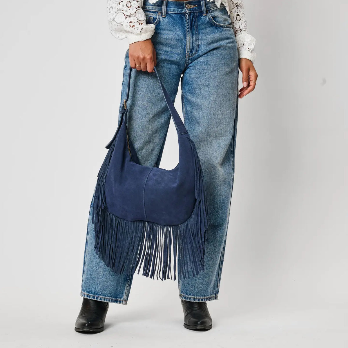 Navy blue suede fringe hobo bag held at side, paired with wide-leg jeans and black boots