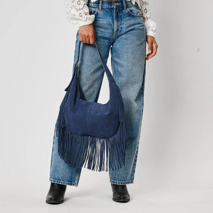 Navy blue suede fringe hobo bag held at side, paired with wide-leg jeans and black boots