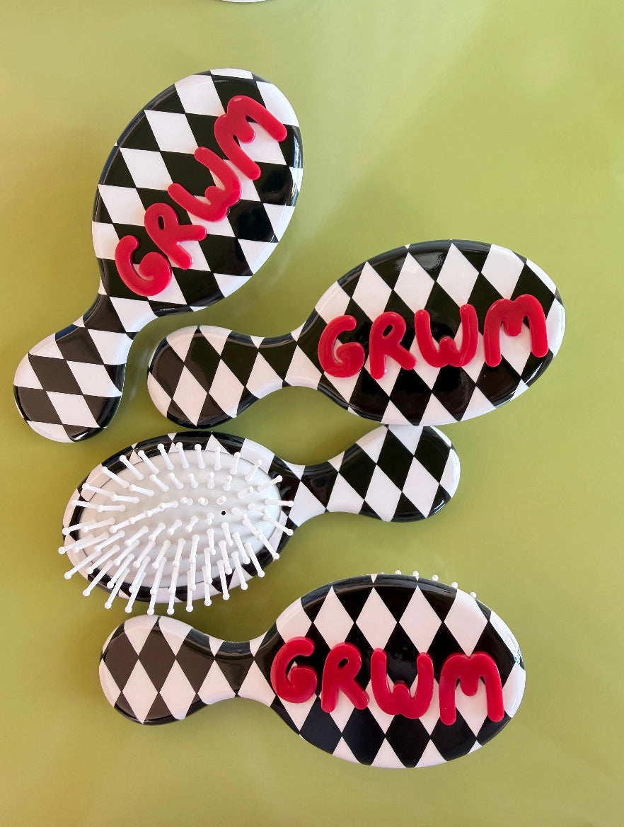 Four black and white diamond checkered mini hair brushes with red GRWM lettering on olive background