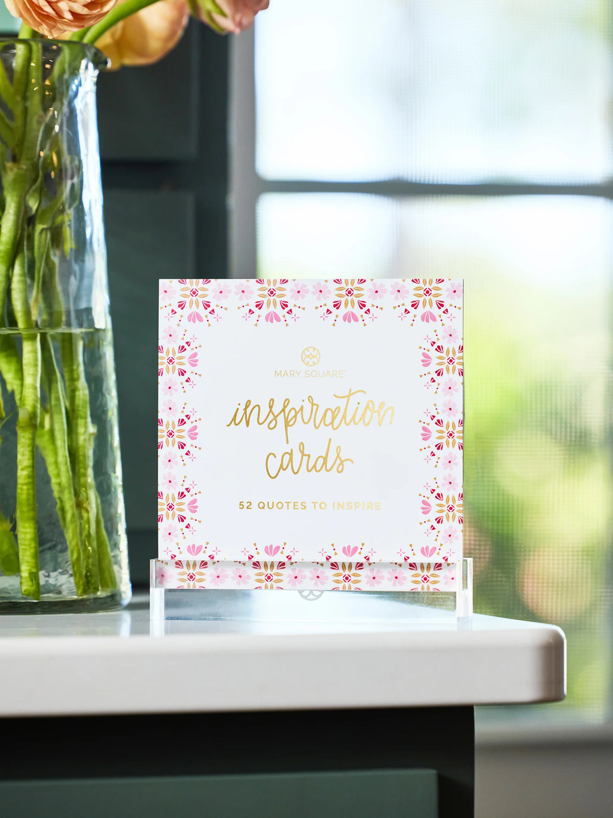 Mary Square Inspiration Cards block in acrylic stand on white table beside glass flower vase
