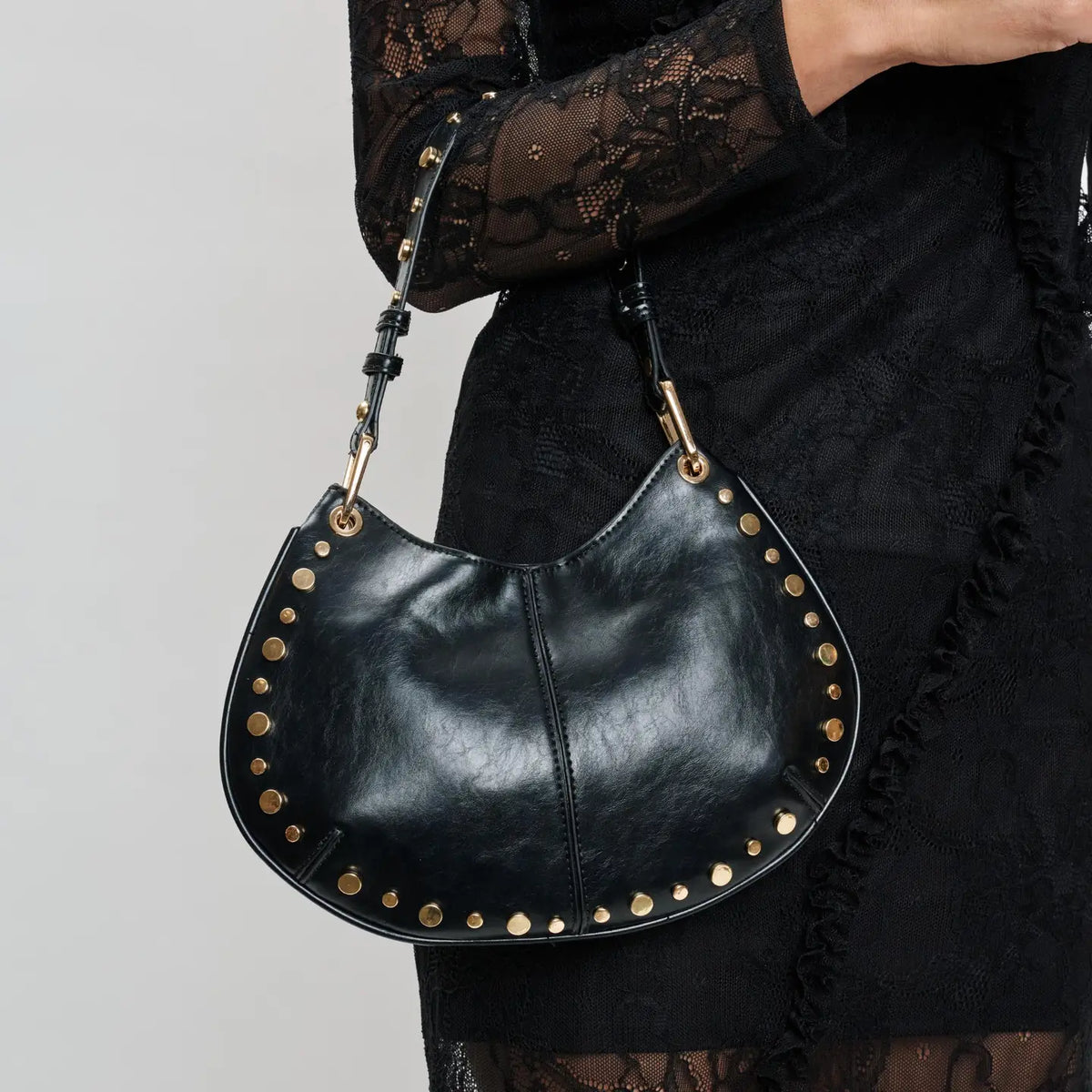 Close-up of black studded leather crescent shoulder bag with gold hardware detail