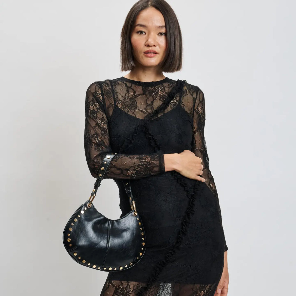 Model in black lace dress holding Moda Luxe Nova black studded crossbody bag