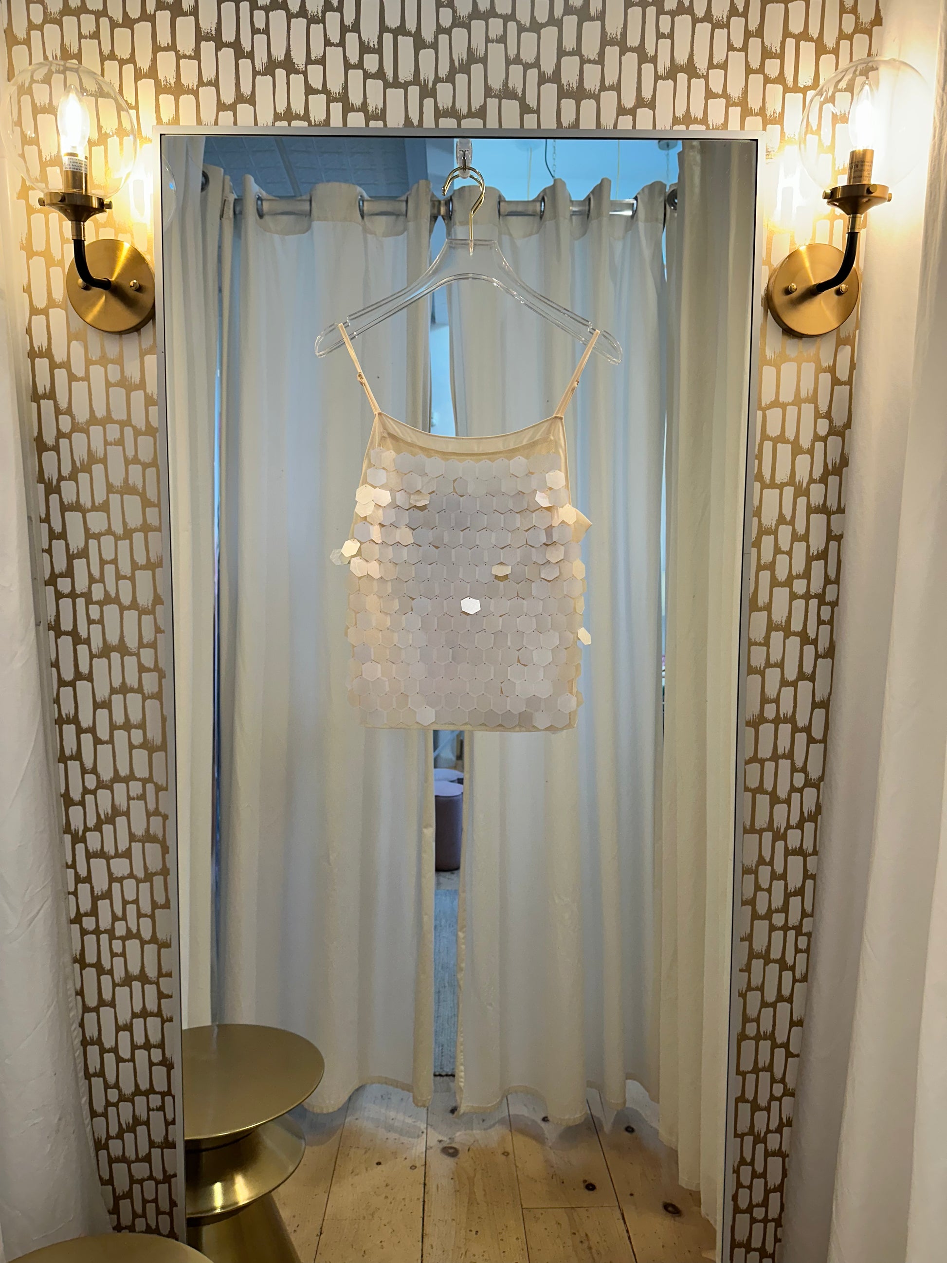Ciebon Ella Sequin Top in ivory, hanging in boutique dressing room with warm lighting