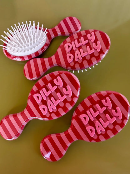 Four red and pink striped mini hair brushes with pink Dilly Dally lettering on olive background
